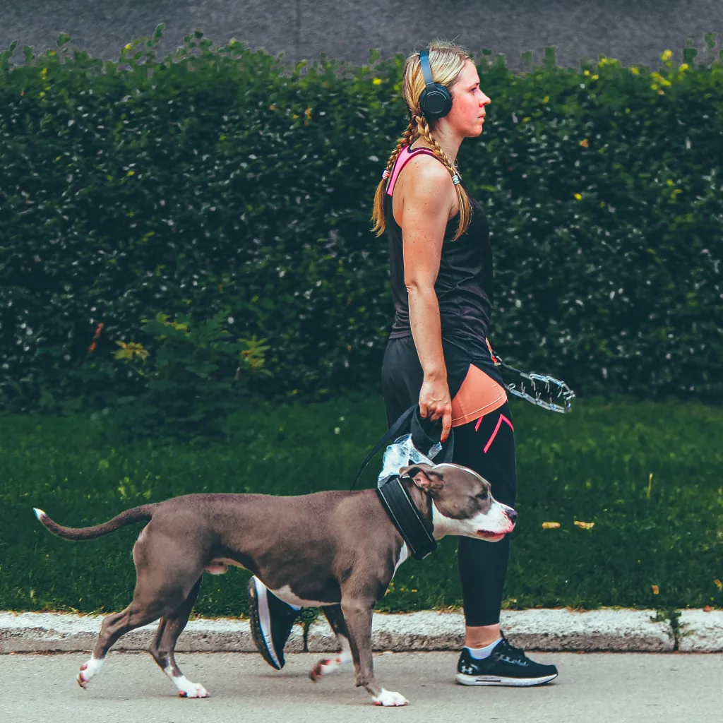 A woman wearing headphones walking a dog on an outdoor path